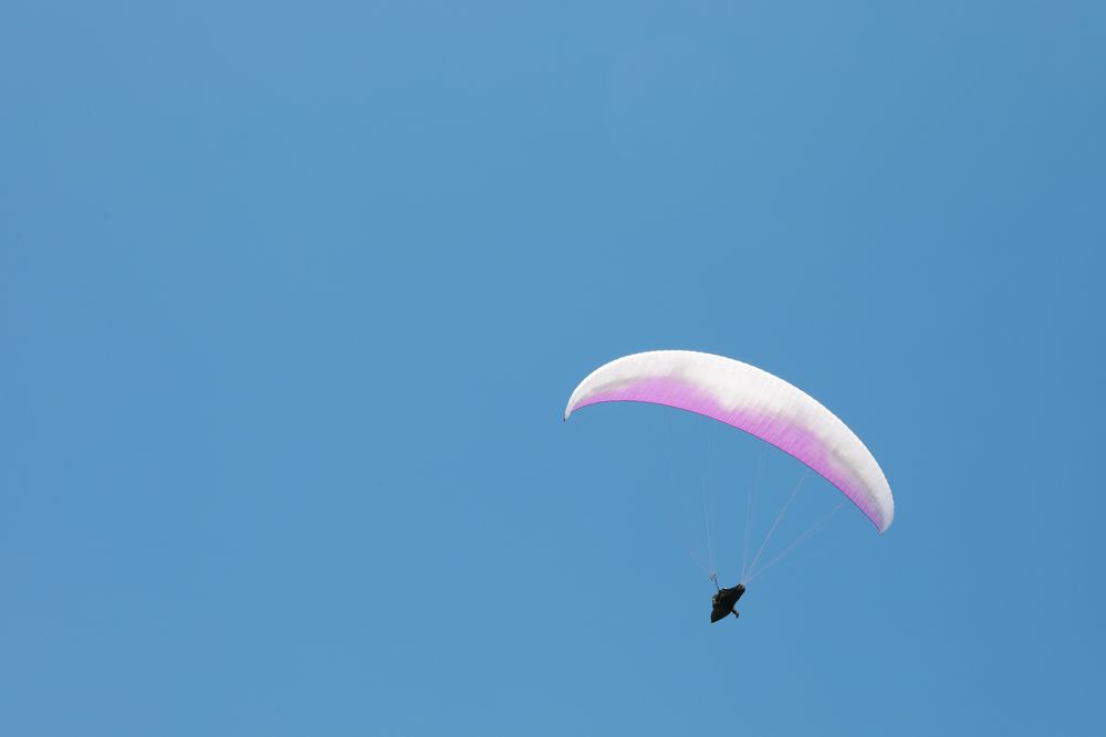 Skydiver with a pink parachute flies across the blue sky
