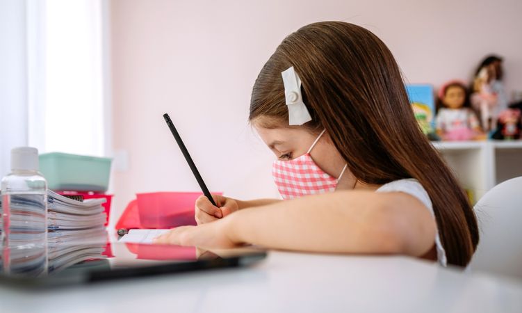 Girl with mask doing homework in her bedroom
