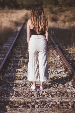 Long haired woman standing on railways overgrown with dry grass