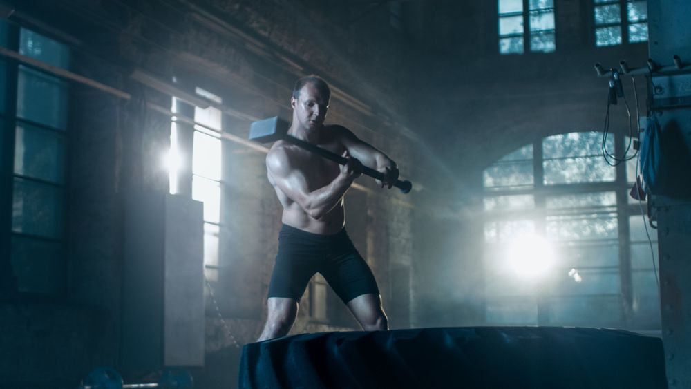 Strong Muscular Man Hits Tire with a Sledgehammer as Part of His Cross Fitness Bodybuilding Gym Training.