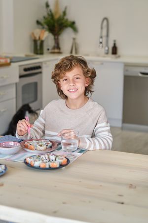 Smiling boy having delicious sushi for lunch at home