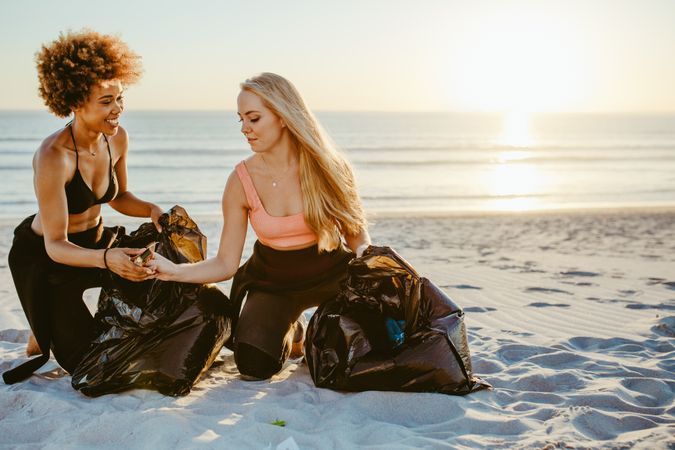 Women surfers cleaning the beach and collecting the litter in garbage bag