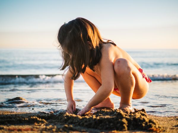 Cute little girl playing with sand at beach
