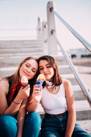 Two young women sitting on the steps outside enjoying ice cream cones