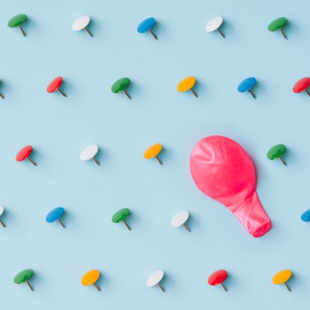 Colorful thumbtacks with deflated balloon on blue background