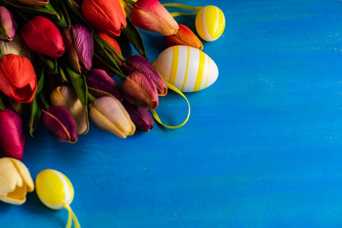 Flat lay of tulip flowers and egg ornaments on blue counter with space for text