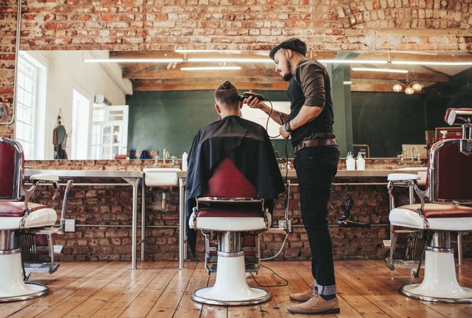 Barber trimming young man’s hair in barbershop