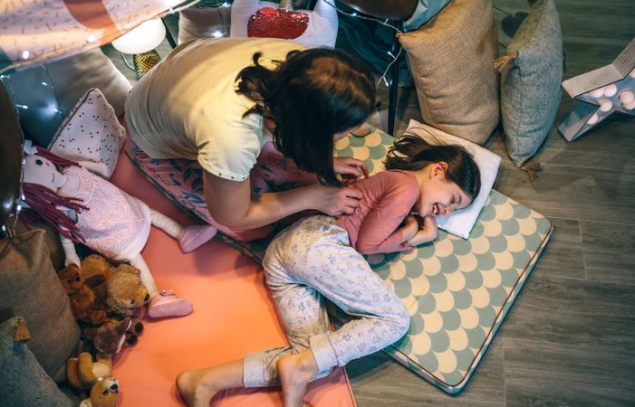 Woman waking up a smiling young girl lying over mats. Single parent family leisure concept.