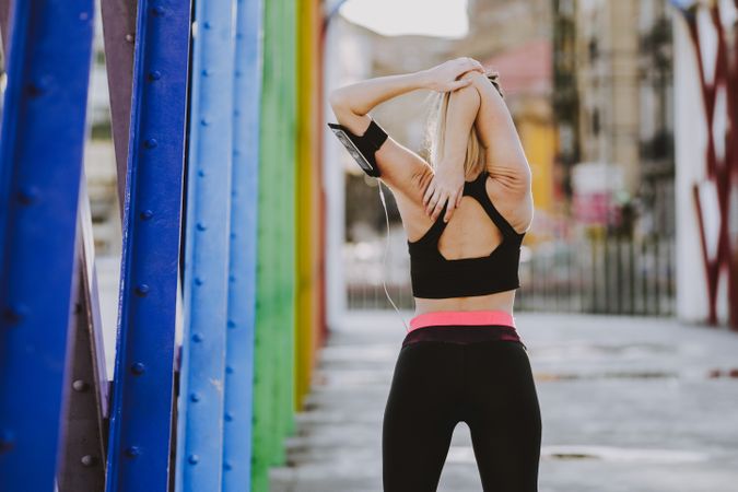 Woman with earphones stretching hands on street