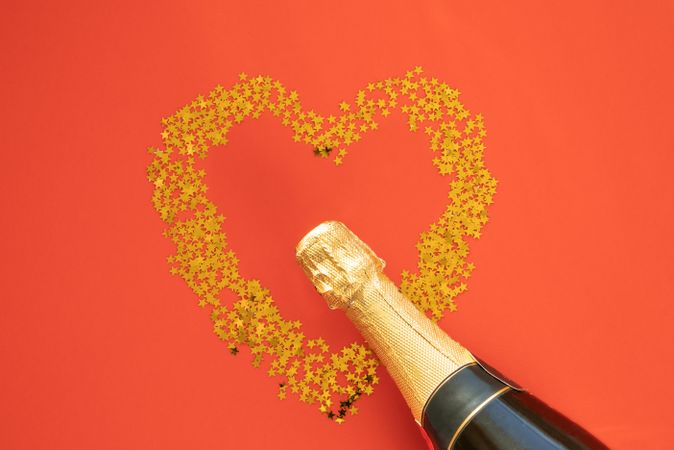 Star shaped glitter arranged in heart shape on orange paper with champagne bottle