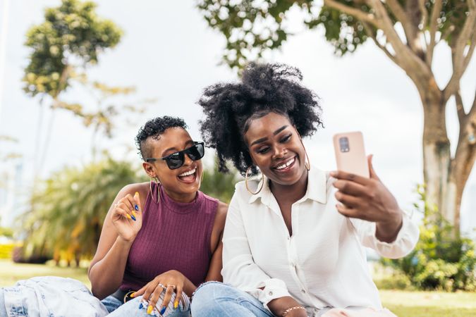 Happy women taking selfies sitting on the grass