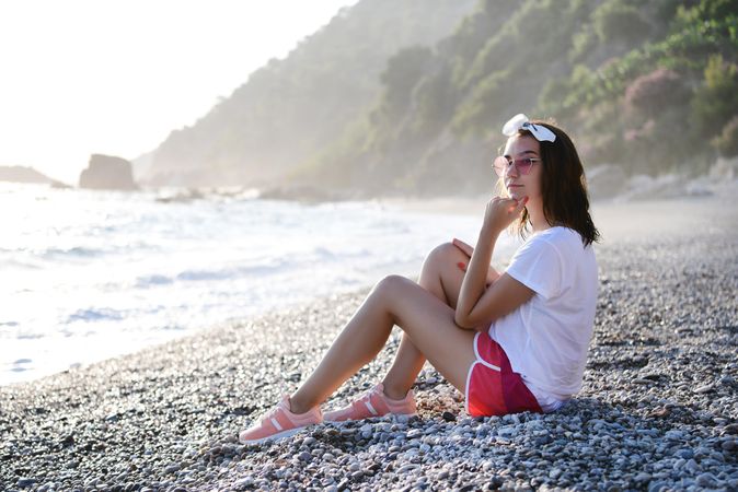 Young woman sitting on pebble beach with contemplative look