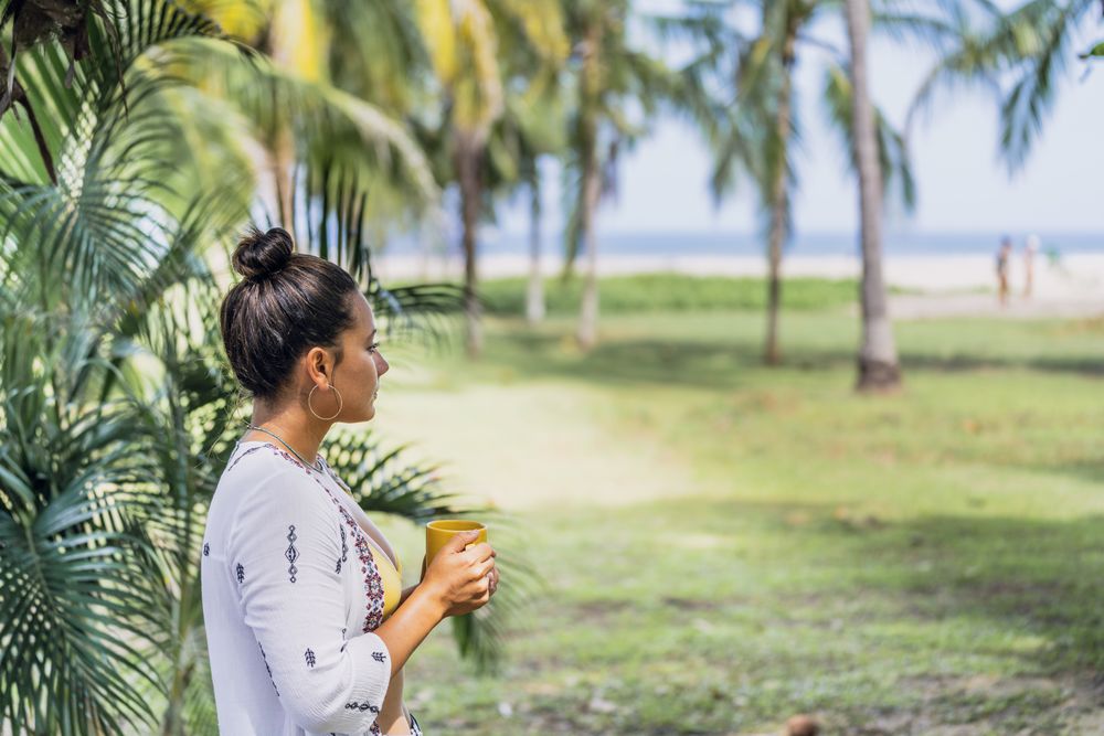 Relaxed woman enjoying hot drink and standing on exotic lawn