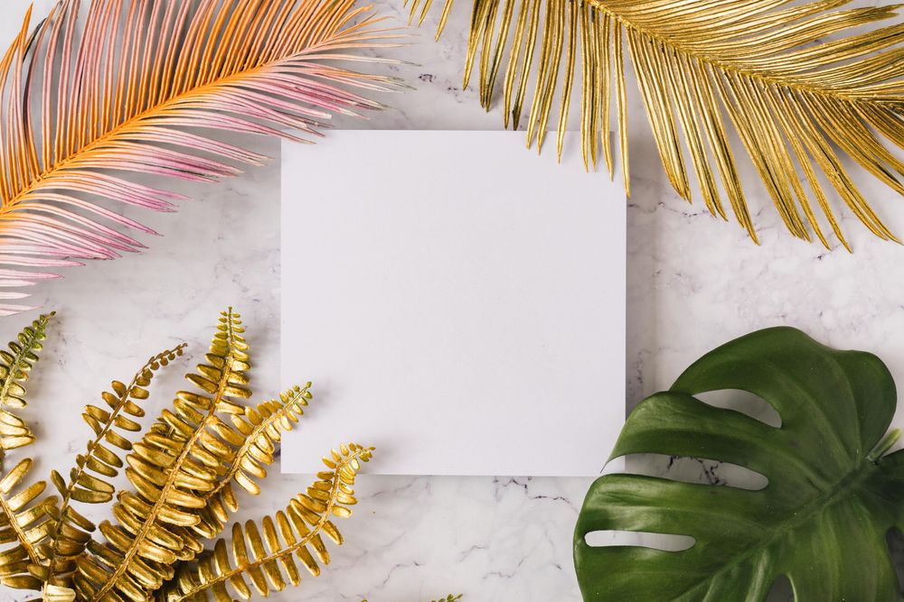Variety of colorful leaves surrounding square paper on marble background