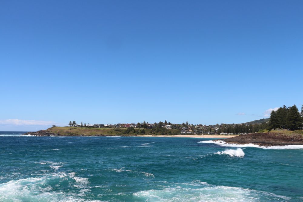 Scenic coastal view of a tranquil bay with gentle waves and clear blue skies in a picturesque town