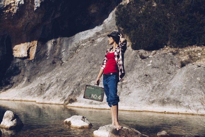 woman standing on rock with case near clear water in lake