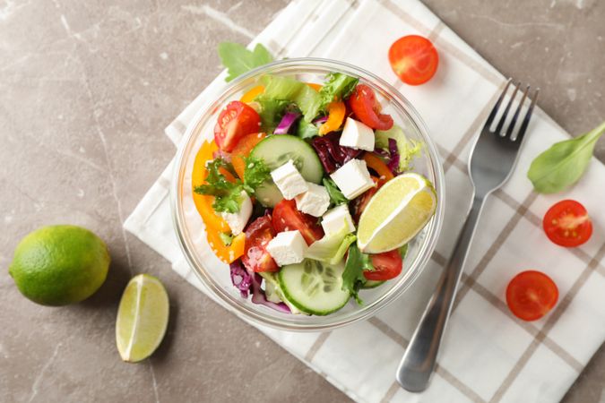 Salad, fork and kitchen towel on grey background, top view