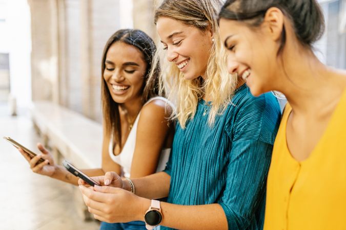 Multi-ethinic female friends laughing while looking at social media content on smartphone