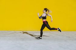 Woman with earphones running near wall