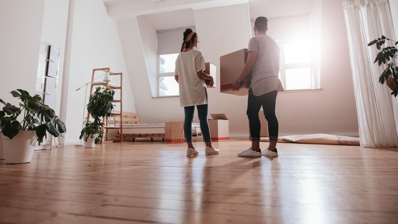 Young man and woman holding packing boxes and moving in new studio apartment
