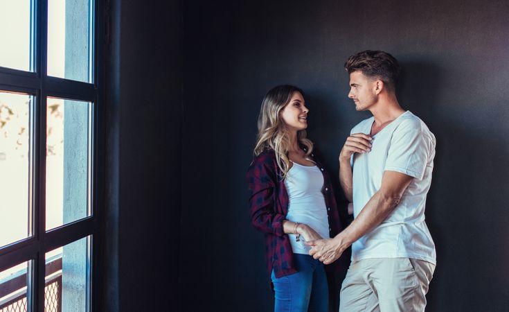 Romantic couple holding hands while leaning against dark wall