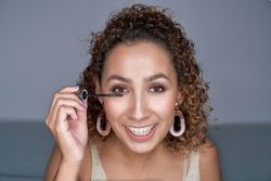 Cheerful young woman applying mascara on eyelashes