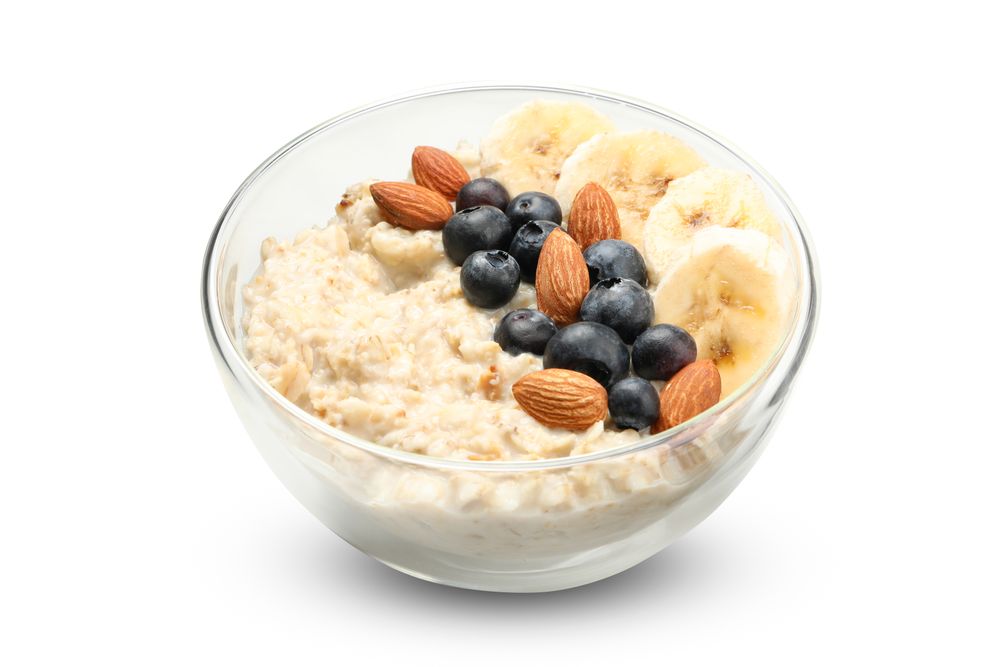 Bowl with oatmeal porridge and ingredients isolated on plain background