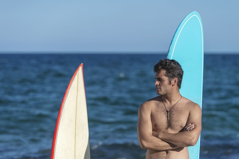 Mid shot of male surfer standing with two boards with ocean in background