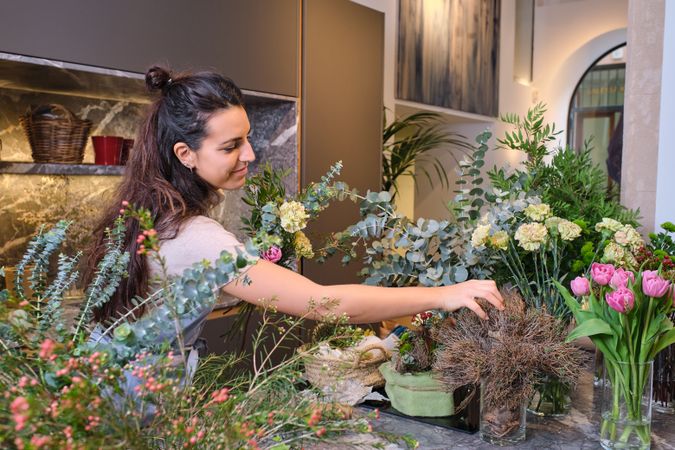 Young woman standing at table with various blooming flowers in f