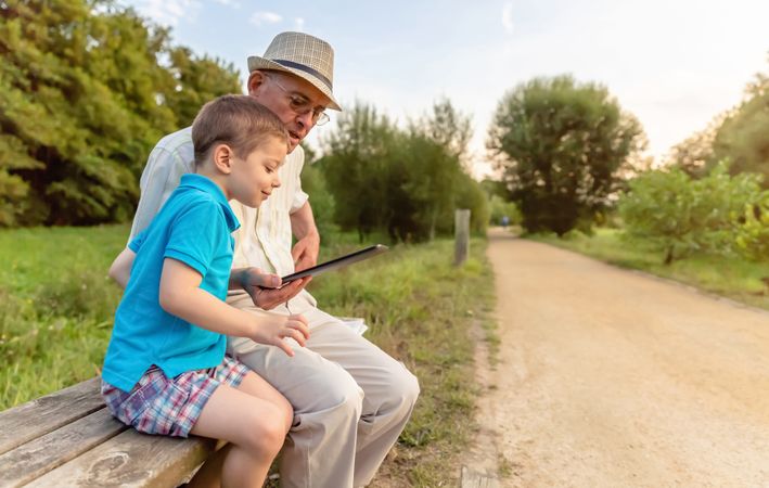 Grandchild and grandfather using a tablet on park bench