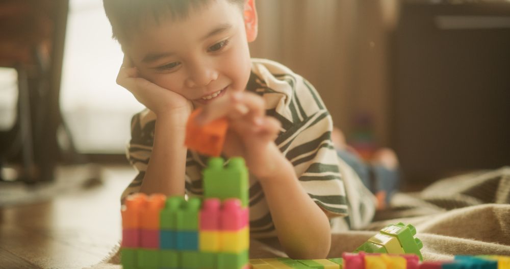 Portrait of Male Asian Kid Playing with Colorful Building Blocks in his Room During the Day.
