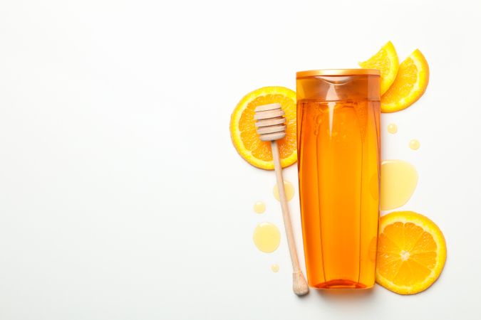Shampoo bottle, orange slices and dipper on light background. Natural cosmetics