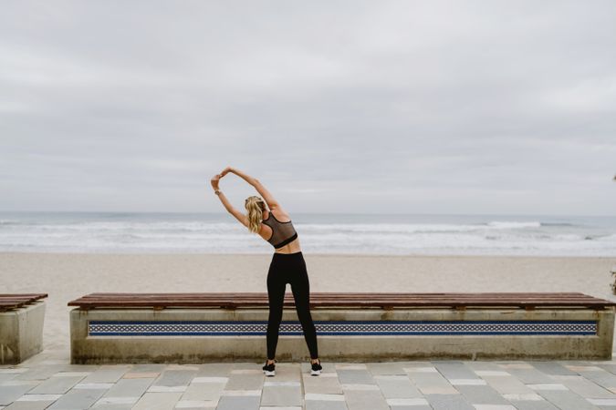Faceless woman gymnast in sports clothing stretching before exercise at seaside