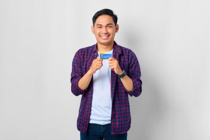 Asian male in grey studio holding up credit card with his hands