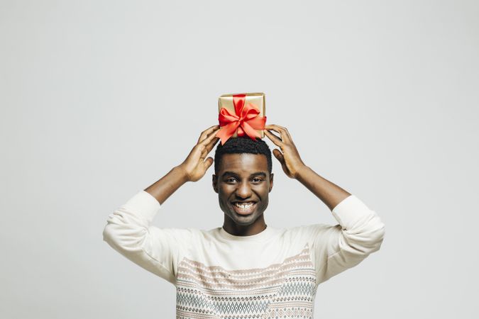 Happy Black man holding gold box with red bow above his head