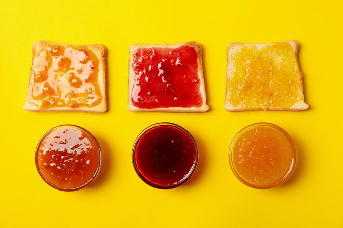 Toasts and bowls with jam on yellow background, top view