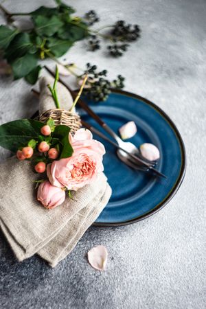 Delicate pink flowers on grey napkin and blue plate with silverware and space for text