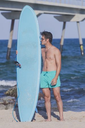 Full body shot of male surfer standing in the rocks on the coast near pier, vertical