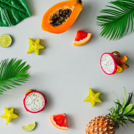 Tropical fruit, pineapple, papaya, dragonfruit on light background with palm leaves
