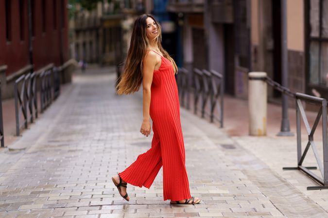 A Fashionable Woman Dressed in a Stunning Red Dress is Walking Through a Lively Urban Alley