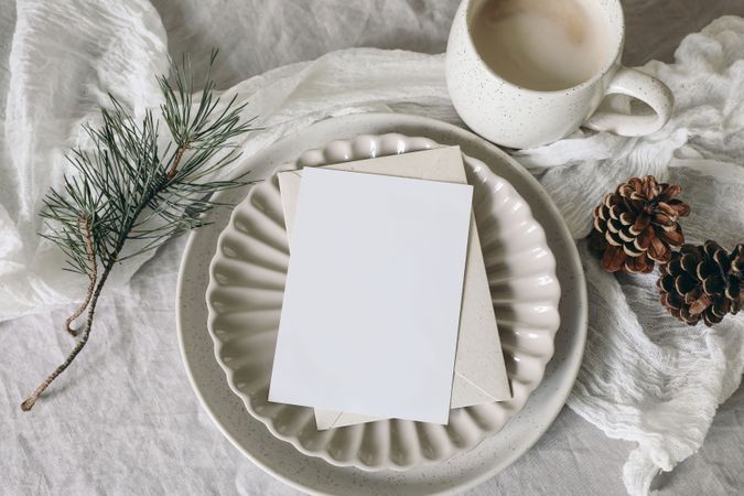 Blank greeting card, invitation mockup on ceramic plate with pine cone and branch on tablecloth