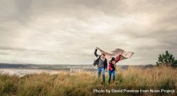 Portrait of loving couple playing outdoors with blanket on a windy day over dark cloudy sky bDyXJ0