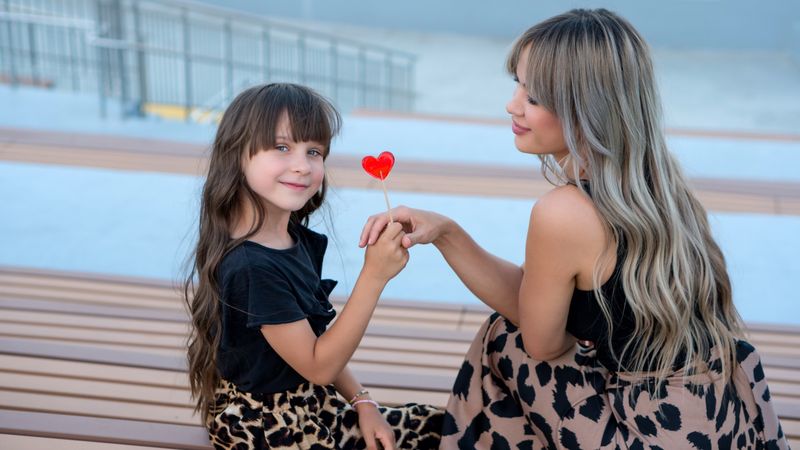 Mom and little daughter with red heart shaped lollipop outdoor
