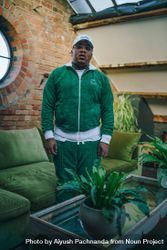 Stylish Black man in green fuzzy track suit standing in industrial loft living room 5RV9O5