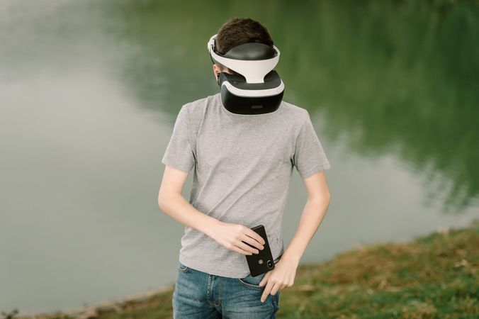 Young teenager with virtual reality glasses and smart phone outdoors