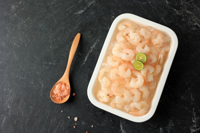 Top view of trey of frozen shrimp with spoon and limes