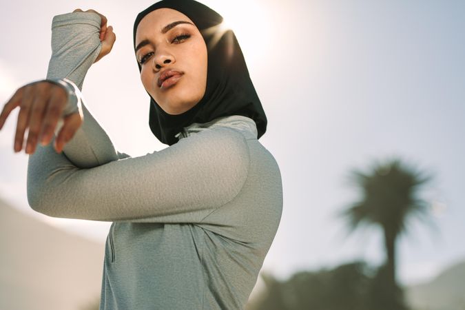 Young sportswoman in hijab stretching her arms and looking at camera