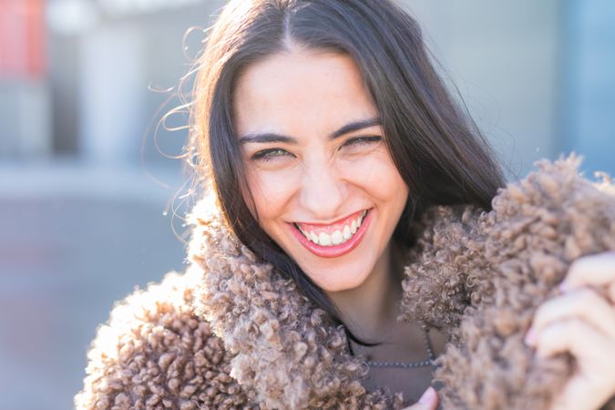 Cheerful woman wrapping in coat on street