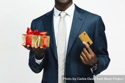 Image of cropped Black man holding present wrapped in gold paper and credit card 4MnREb