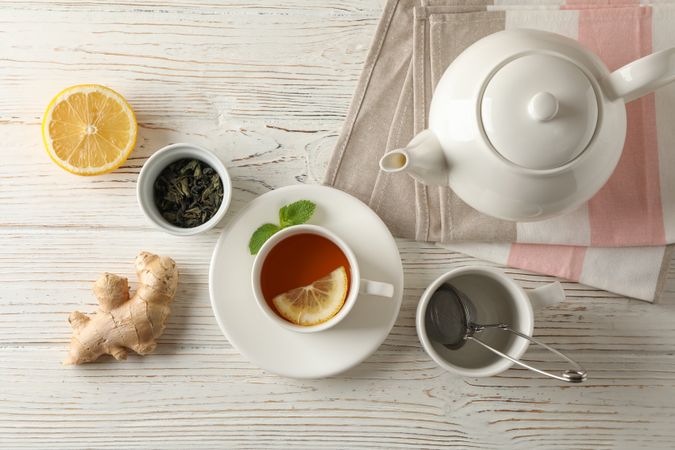 Cup of tea with lemon, mint, strainer, ginger and teapot on wooden background, top view